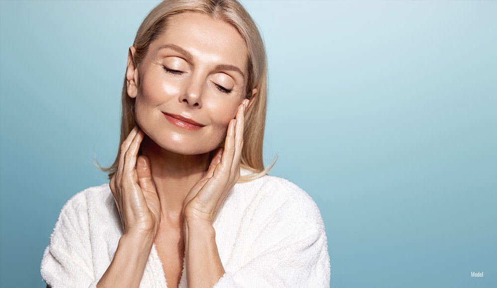 Senior woman with smooth, glowy skin closing her eyes and touching her face with both hands.