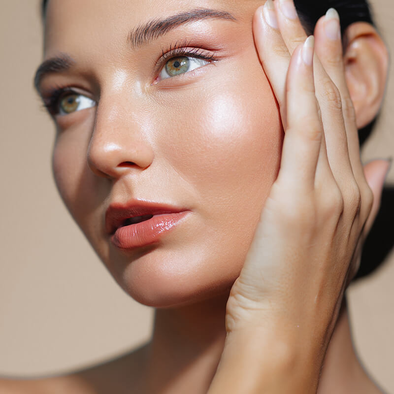 Young woman with glowing skin touching her face