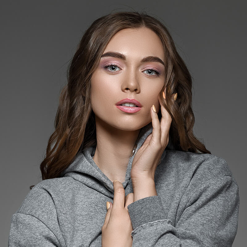 Young woman in a gray sweater touching her face